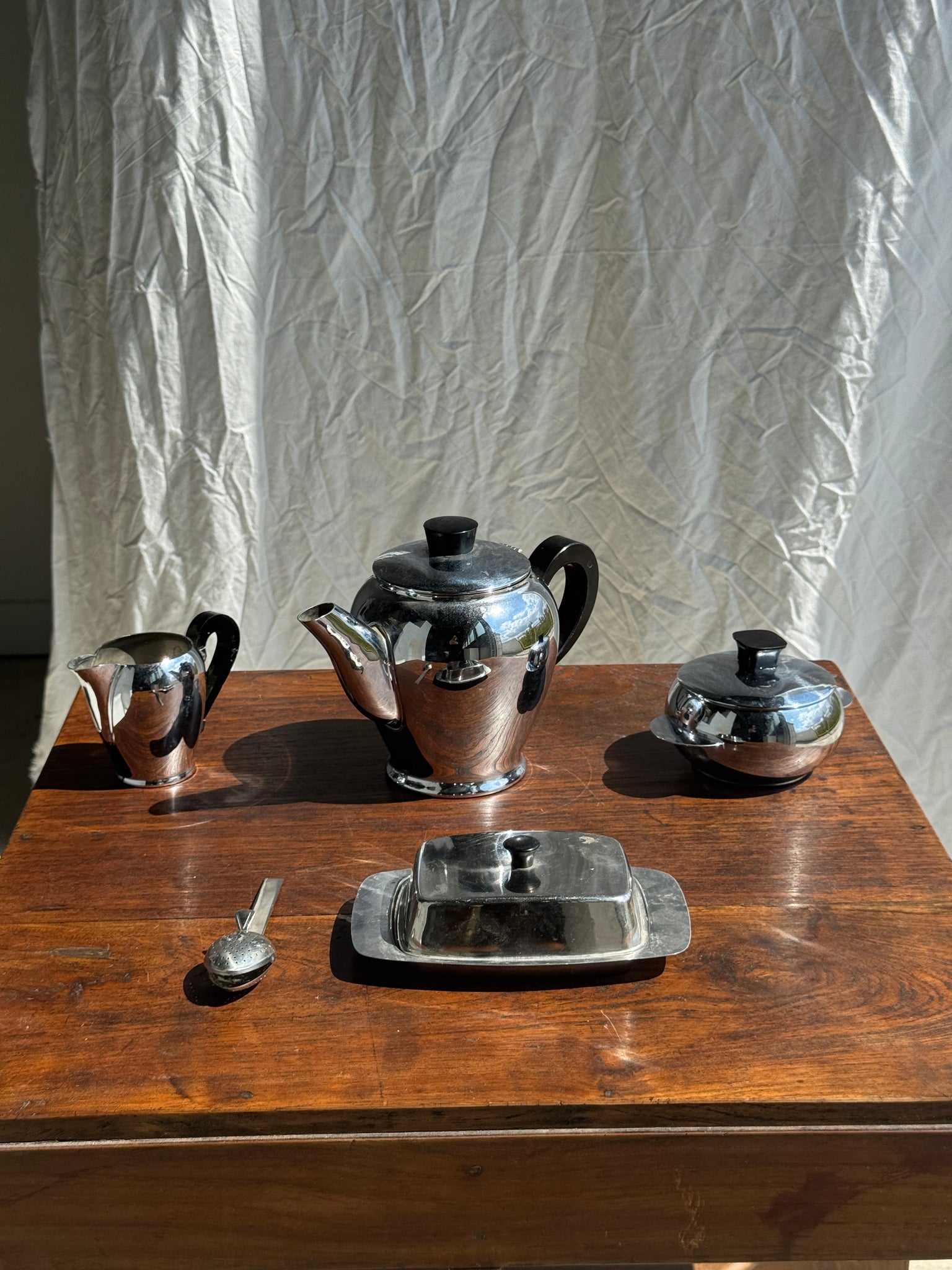 Service à thé comprenant une théière, un pot à lait, un sucrier et un beurrier en métal argenté et poignées noires